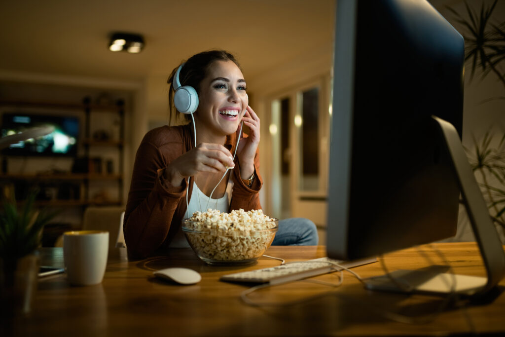 Young woman having fun while eating popcorn and watching movie o