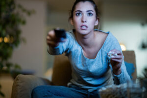 Shocked woman changing channels while watching TV at night.