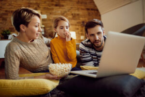 Family using laptop while eating popcorn and relaxing at home.